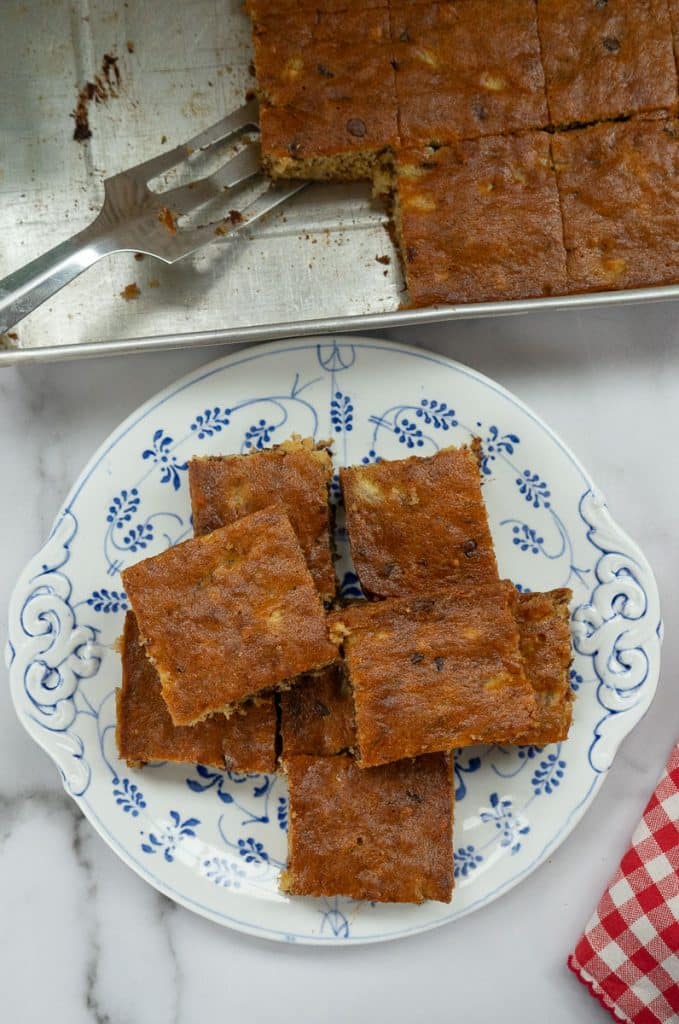 pieces of banana snack cake stacked on a plate with the pan of cake above it in the photo