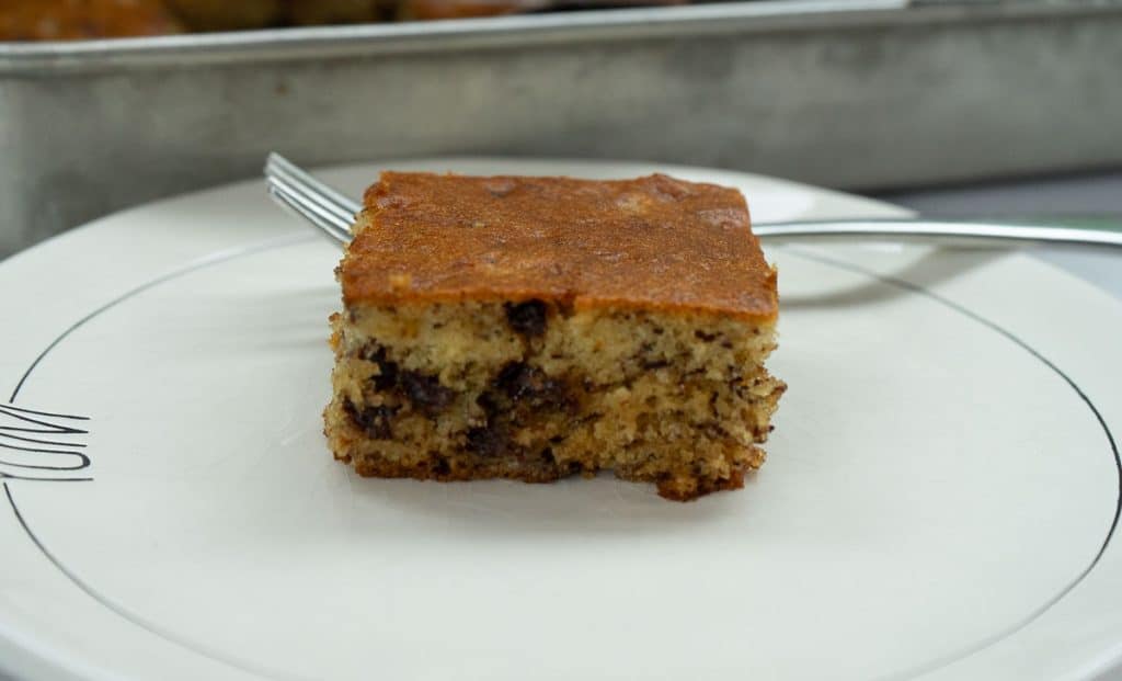a piece of banana cake on a plate in front of the pan of banana cake