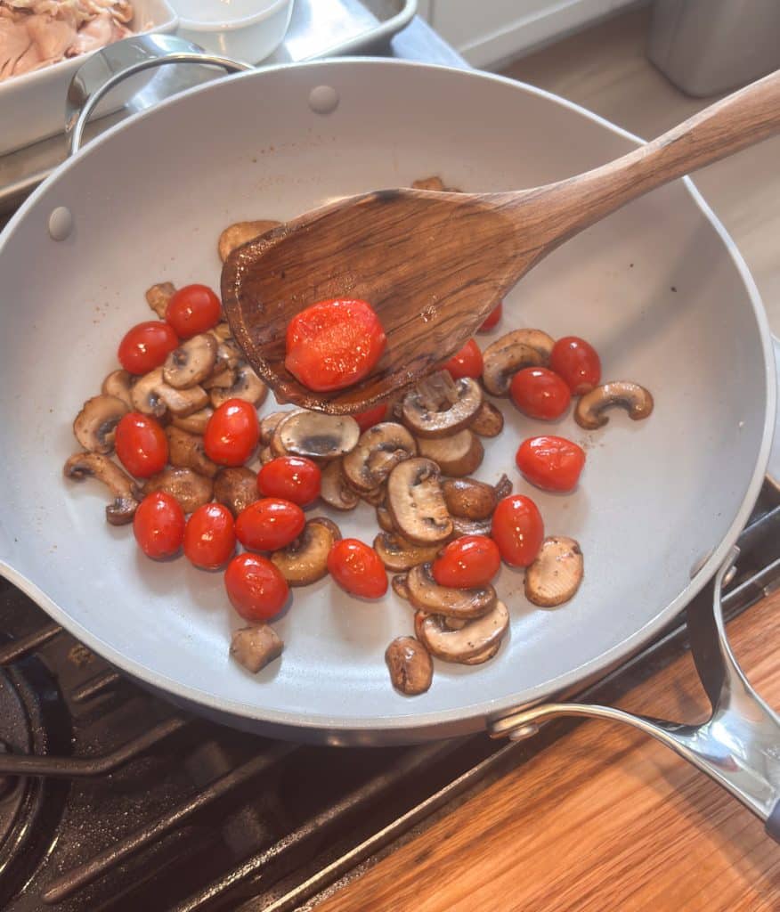 portobello mushrooms and cherry tomatoes in a large skillet with a wooden spoon