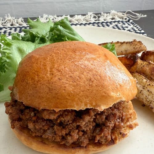 photo of a sloppy joes on a hamburger bun on a plate with salad and potato wedges also on the plate