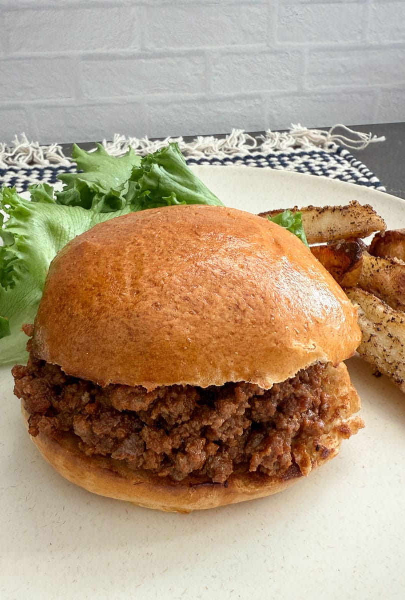 photo of a sloppy joes on a hamburger bun on a plate with salad and potato wedges also on the plate