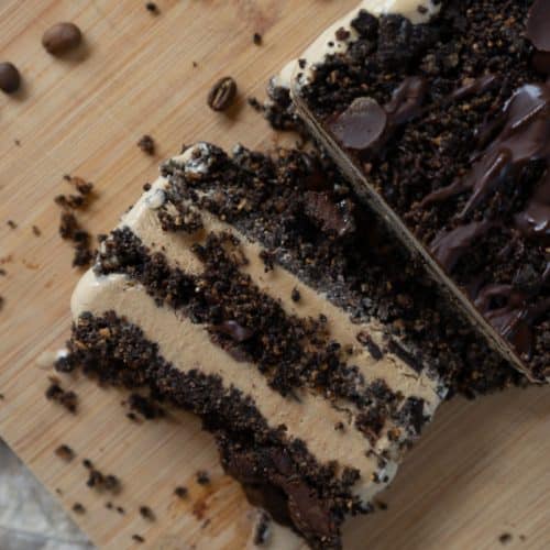Coffee ice cream dessert on a wood plank with coffee beans strewn around and a slice of dessert laying next to the dessert