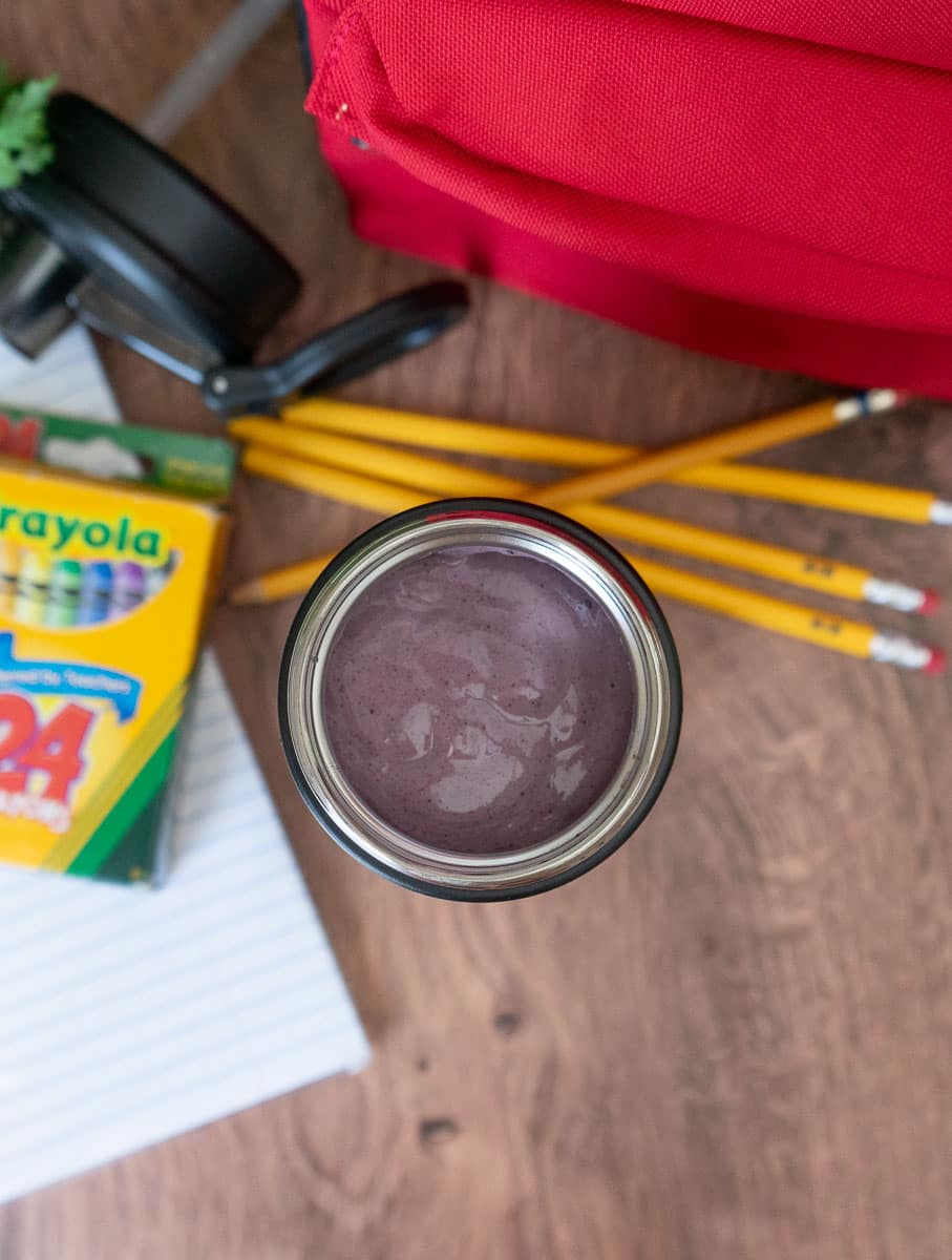 top view of a smoothie in a thermos on a wood counter top with school supplies and a lunch box around it
