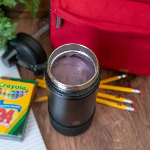 lunch smoothie in a thermos next to a lunch box and school supplies on a wood countertop