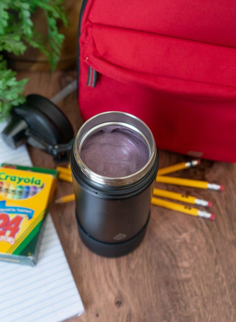 lunch smoothie in a thermos next to a lunch box and school supplies on a wood countertop