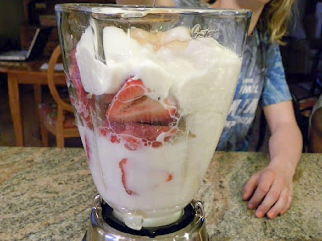 all the ingredients in a blender with a kid in the back ground 