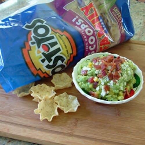 dish of guacamole on a wood cutting board with an open bag of tortilla chips