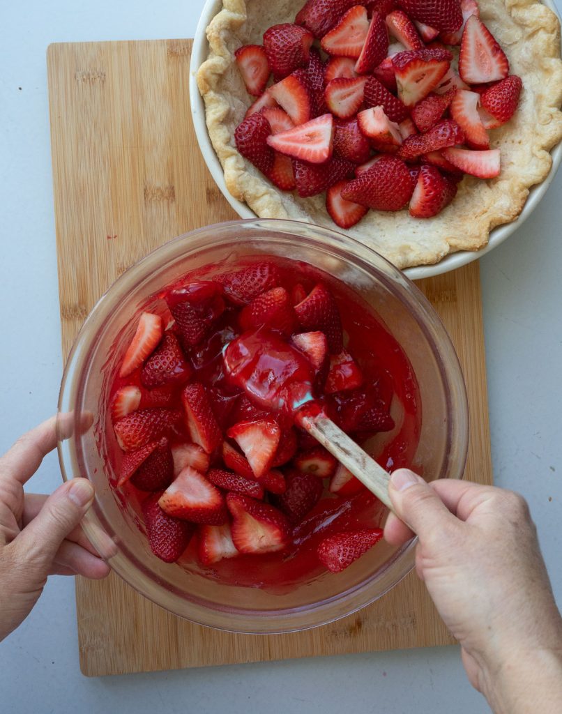 mixing strawberries into glaze, pie crust with cut strawberries is above the bowl