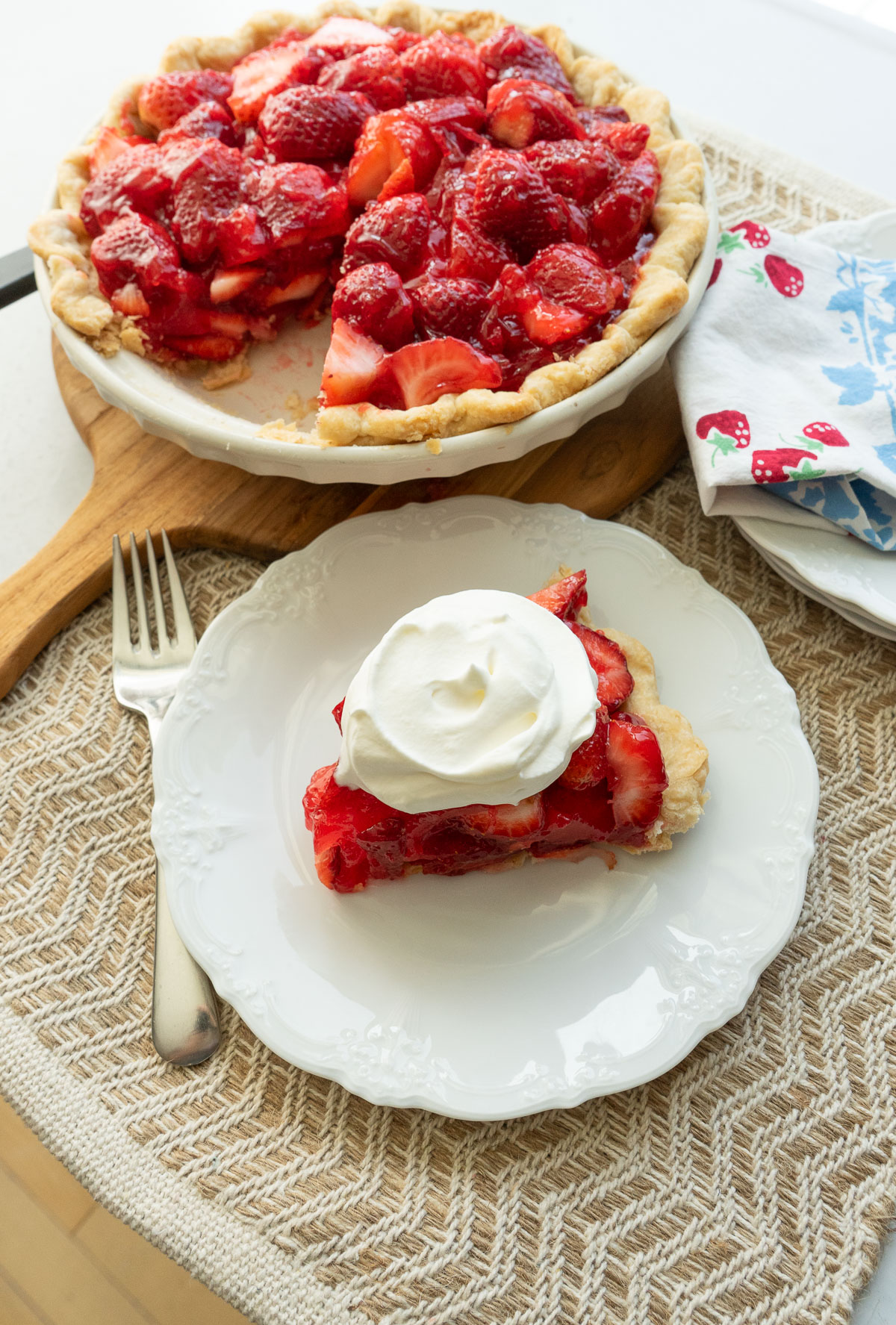Strawberry pie white plate with a piece of strawberrry pie on it with a fork on the left side