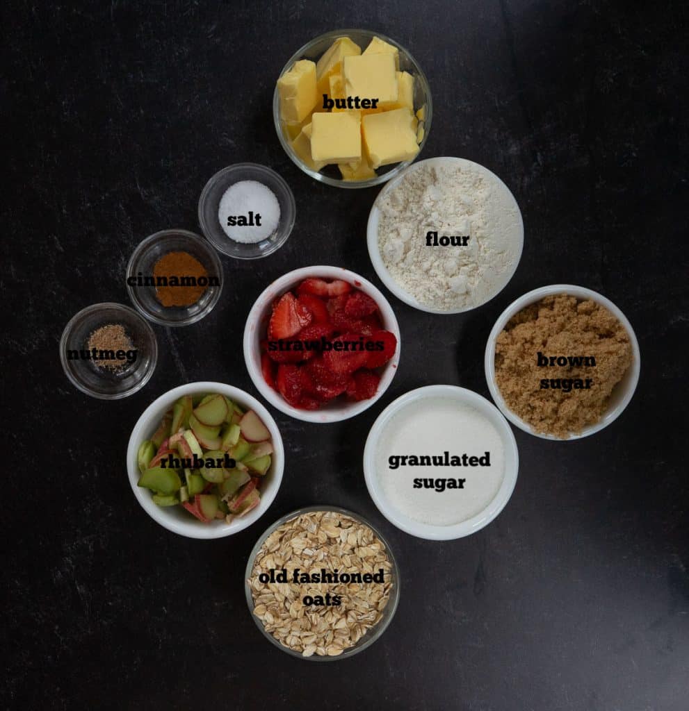 ingredients for strawberry rhubarb crisp on a black surface