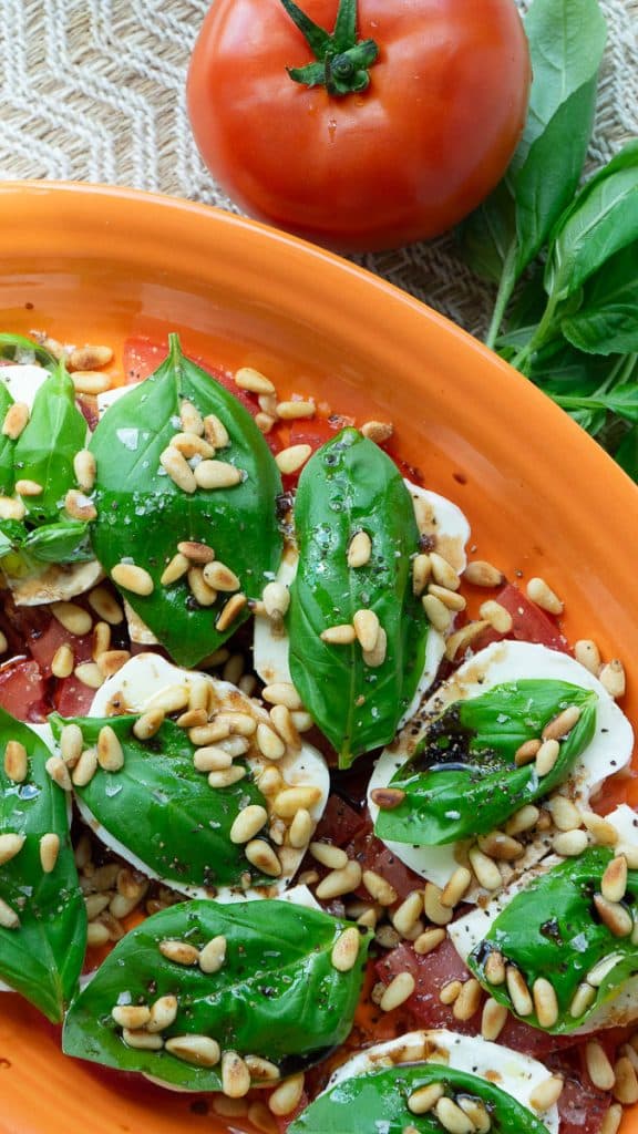 plate of caprese salad, tomatoes layered with mozzarella, basil, pine nuts, olive oil, and balsamic