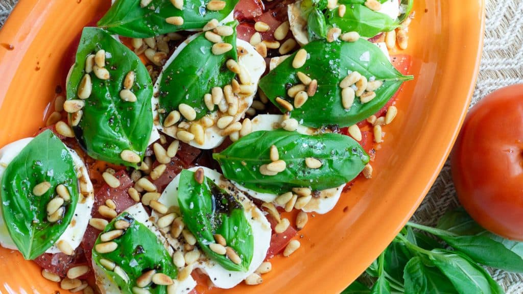 plate of caprese salad, tomatoes layered with mozzarella, basil, pine nuts, olive oil, and balsamic