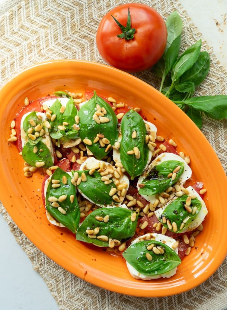 plate of caprese salad, tomatoes layered with mozzarella, basil, pine nuts, olive oil, and balsamic