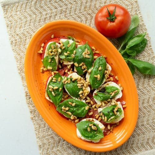 plate of caprese salad, tomatoes layered with mozzarella, basil, pine nuts, olive oil, and balsamic