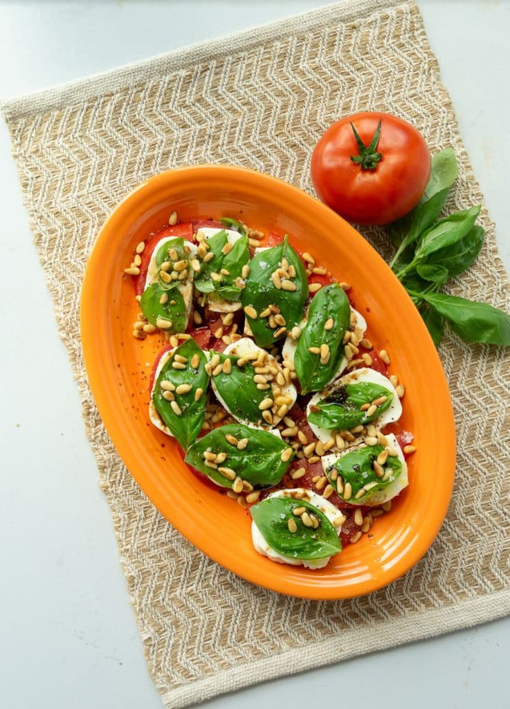 plate of caprese salad, tomatoes layered with mozzarella, basil, pine nuts, olive oil, and balsamic
