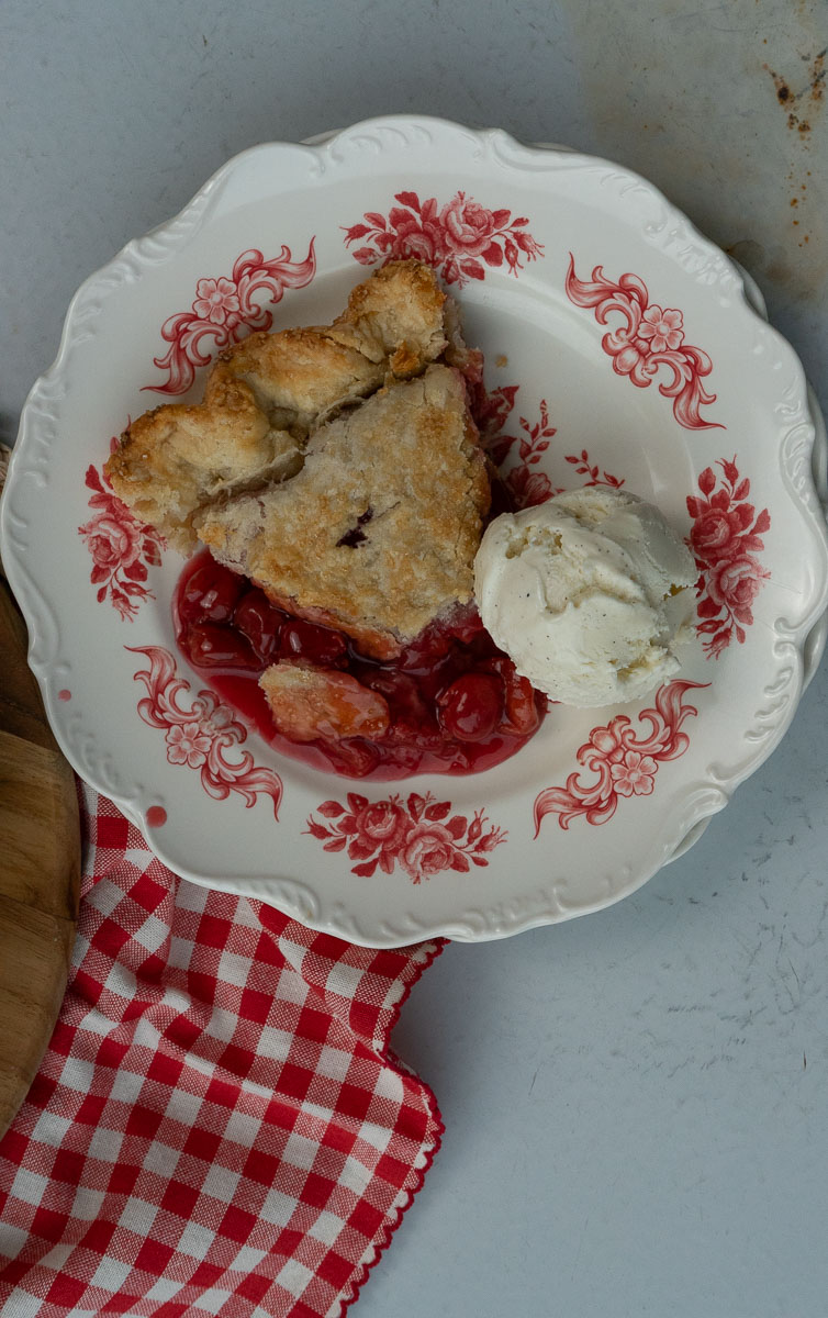 slice on cherry pie on a plate with vanilla ice cream