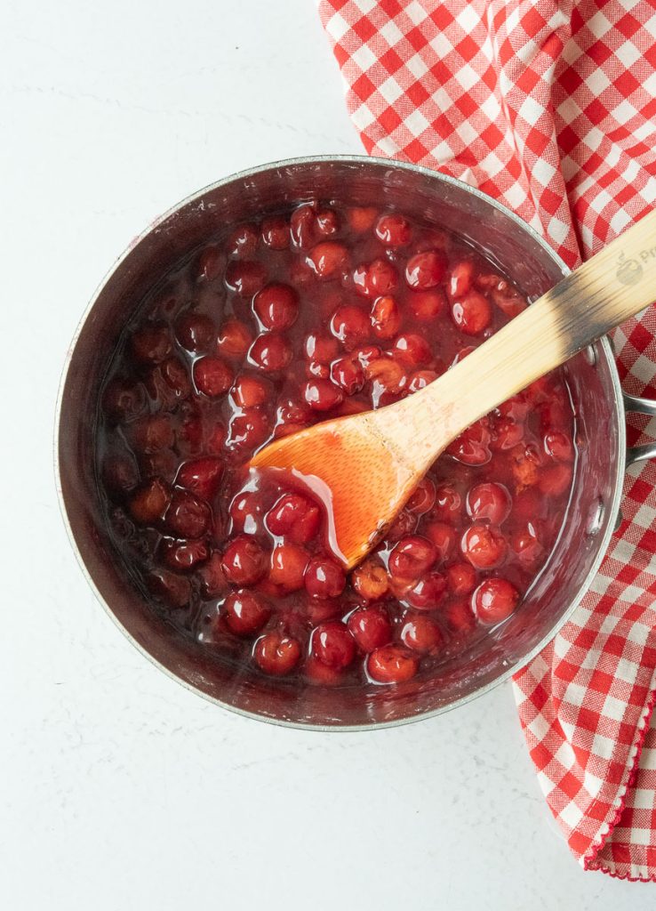cherries cooking in a sauce pan with a wooden spoon