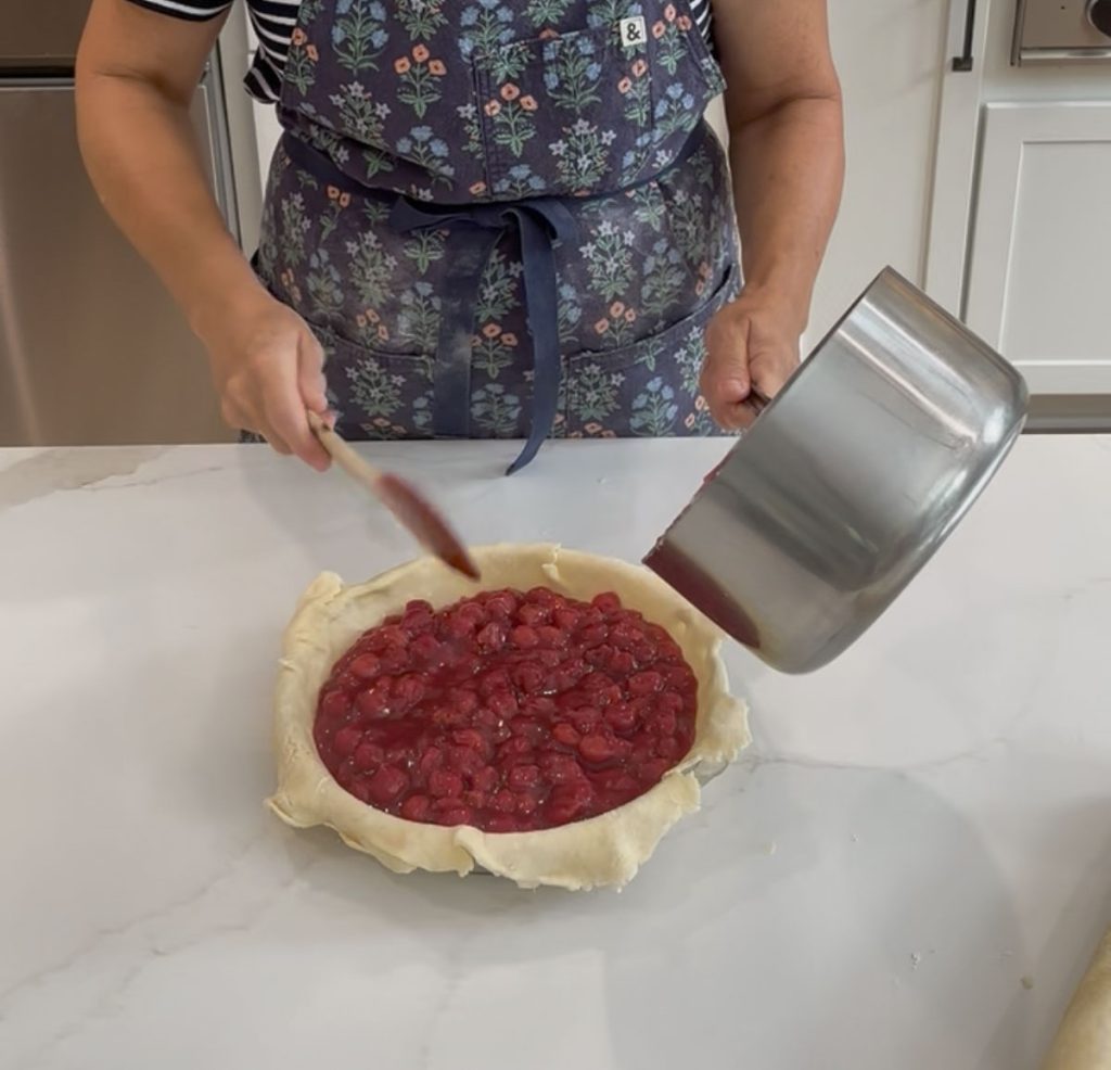 pouring cherry filling into the bottom pie crust