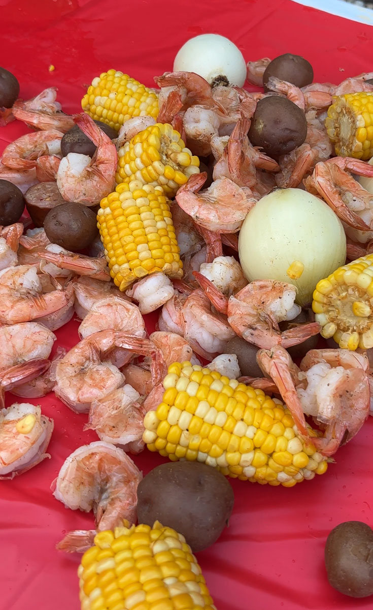 sweet corn, shrimp, red skin potatoes, and onions on a red table cloth, cooked shrimp boil out on table ready to eat