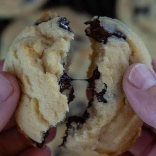 hands breaking apart a warm chocolate chip cookie over a sheet of chocolate chip cookies