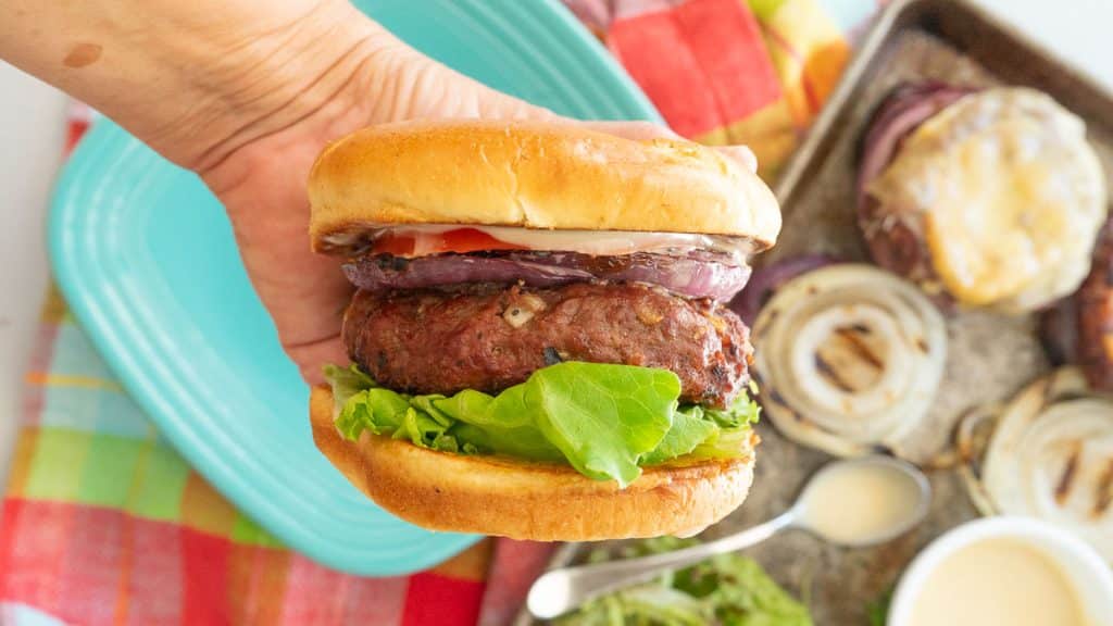 hand holding a hawaiian hamburger with plate and condiments in the background