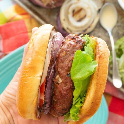 hand holding a hawaiian hamburger with plate and condiments in the background