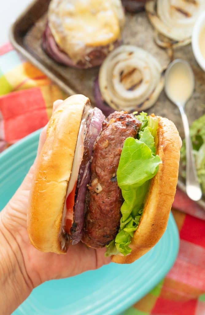 hand holding a hawaiian hamburger with plate and condiments in the background