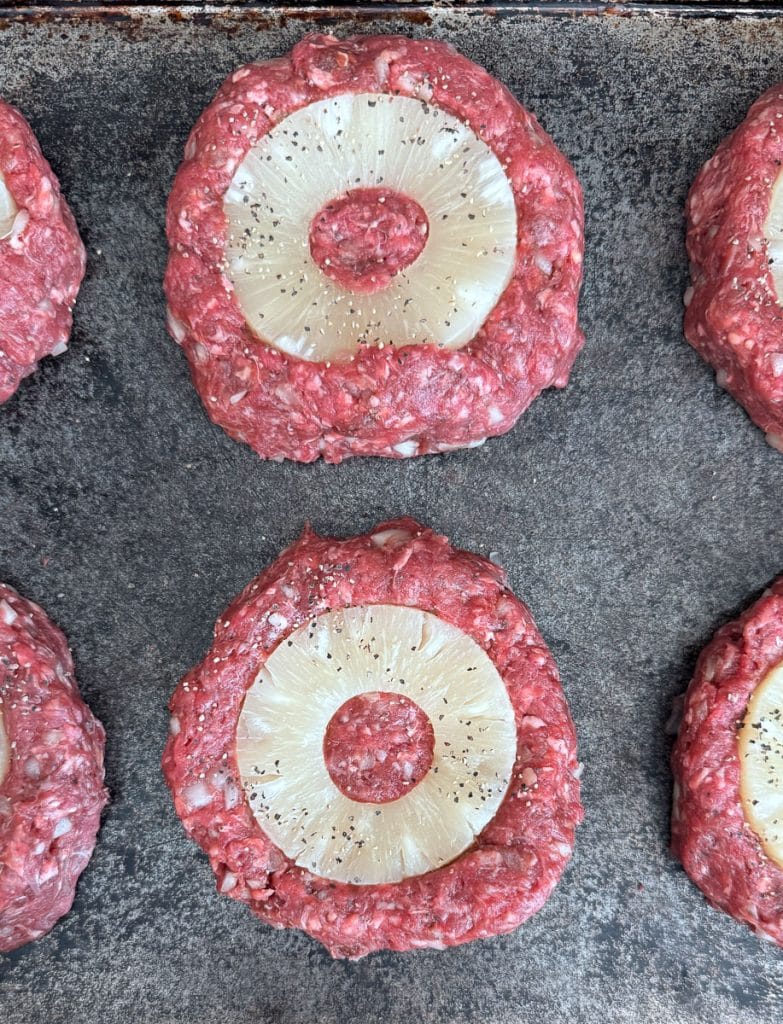 raw hamburger patties with a pineapple slice in each burger