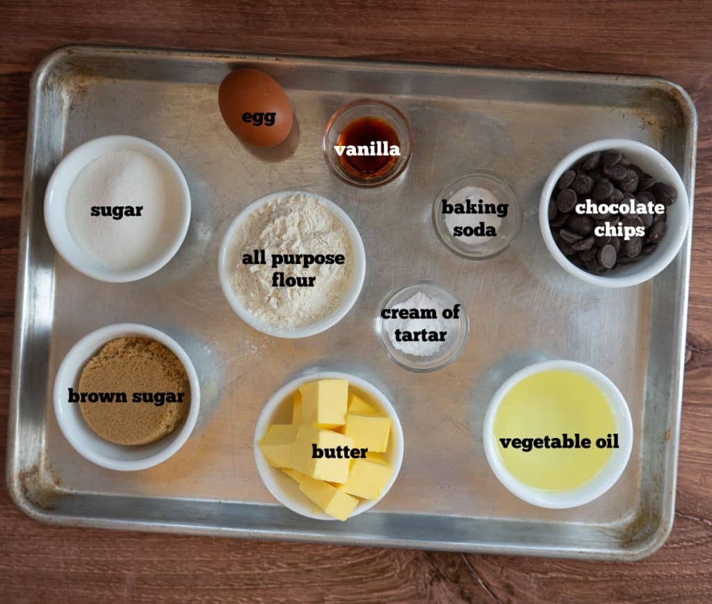 ingredients for melt in your mouth chocolate chip cookies on a baking sheet that is sitting on a wood countertop