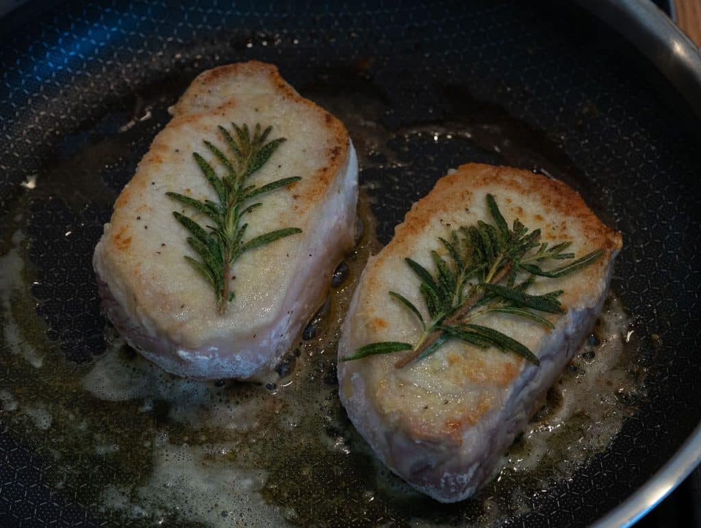 pork chops on stove top being seared in butter