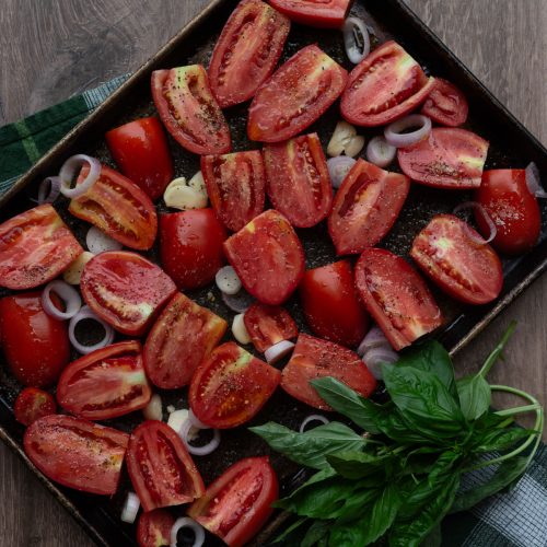 roma tomatoes on a baking sheet with garlic, shallot, olive oil, salt and pepper