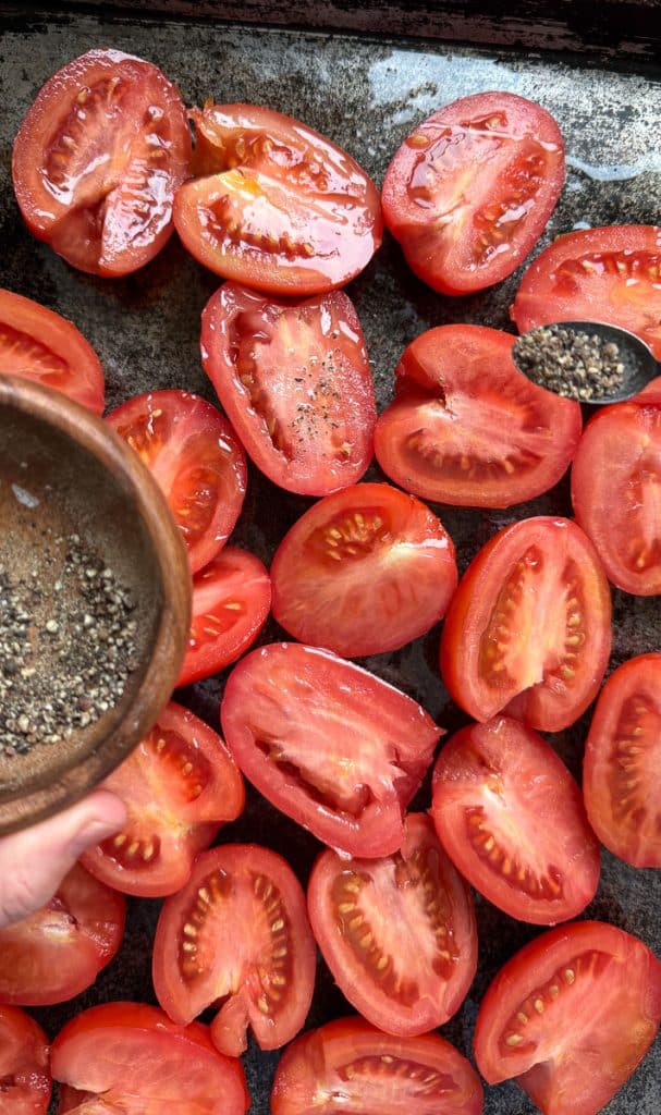 IMG_1704 sprinkling pepper over sliced tomatoes on a baking sheet
