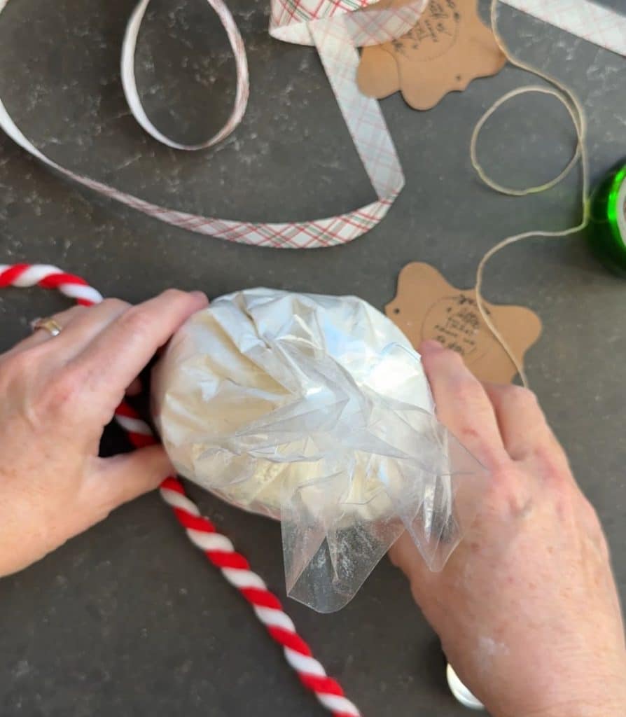 plastic bag of beer bread dry ingredients on countertop with christmas wrappings on the counter and two hands lifting it up