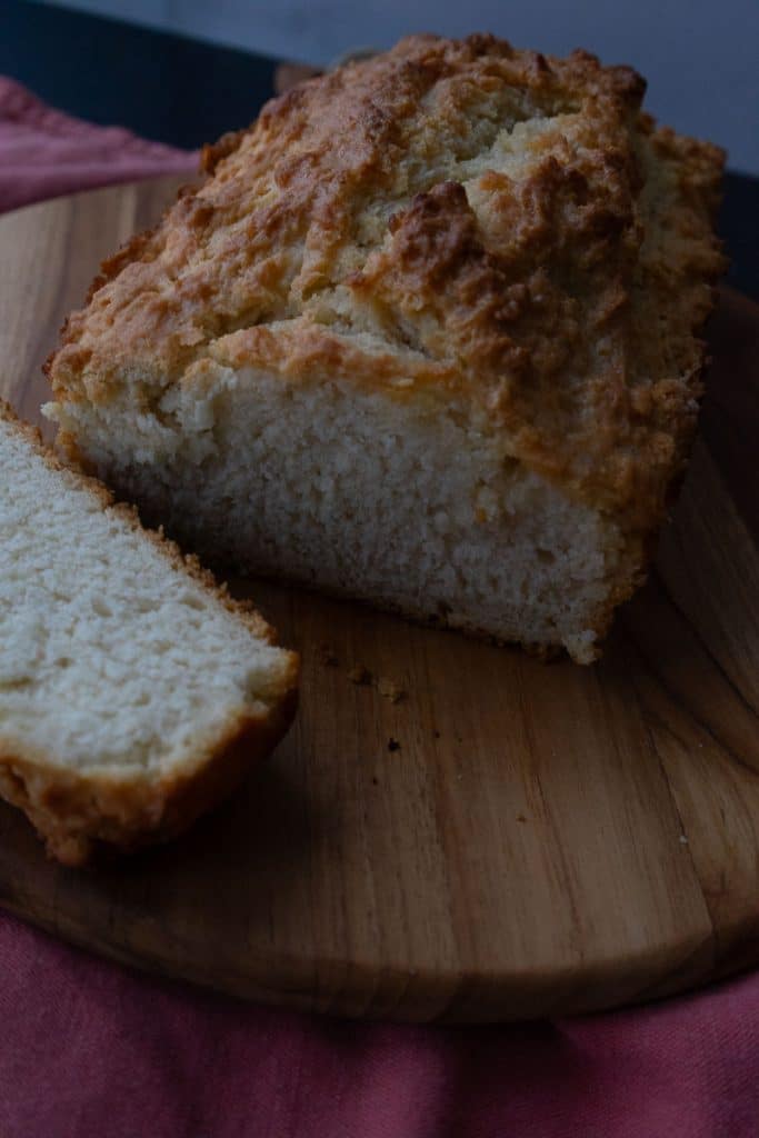loaf of beer bread on a wood cutting board with a slice cut off and laying beside thee bread