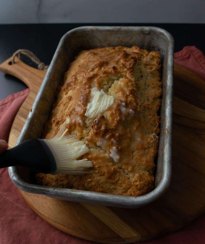 brushing butter over the top of the baked loaf of beer bread with a pastry brush