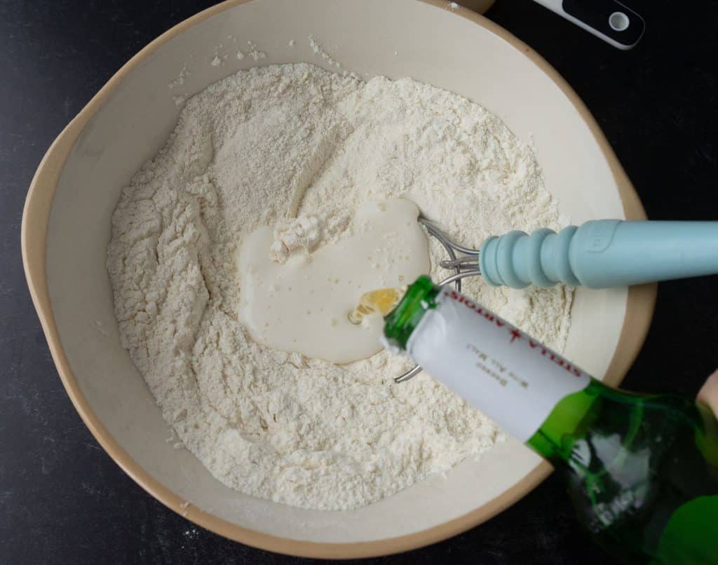 pouring beer into dry ingredients in glass bowl with whisk setting in the bowl