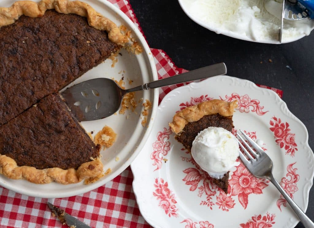 toll house cookie pie with a piece removed beside a piece of toll house cookie pie on a dessert plate with ice cream on top