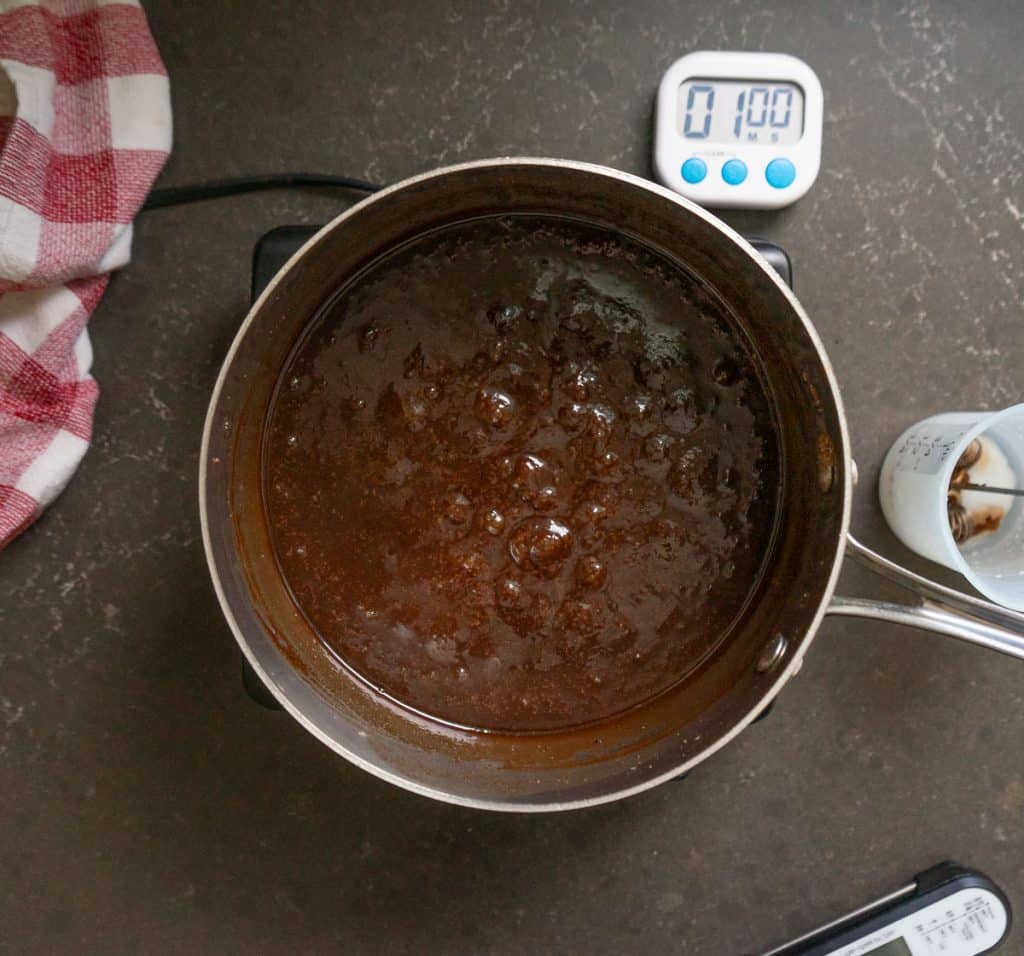 chocolate cooking at a low boil in sauce pan, there is a timer in the upper right hand corner of the picture 