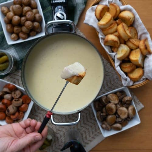 Chunk of bread covered in cheese over a fondue pot full of cheese fondue
