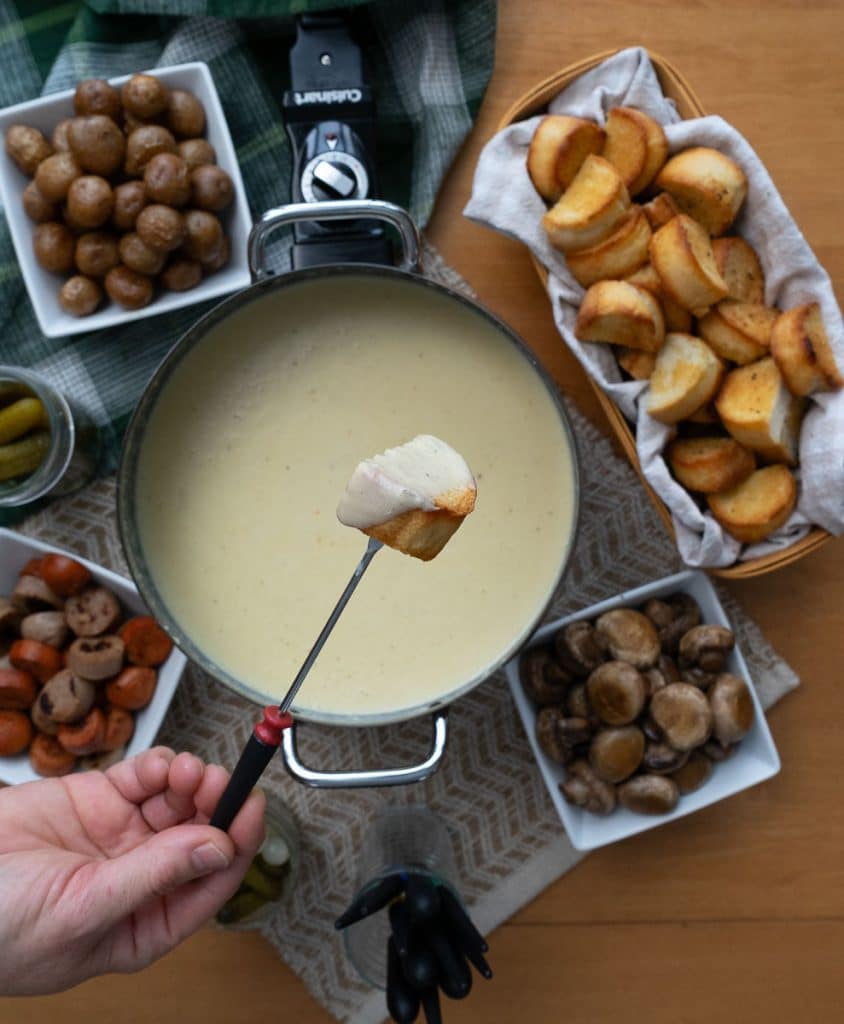 Chunk of bread covered in cheese over a fondue pot full of cheese fondue