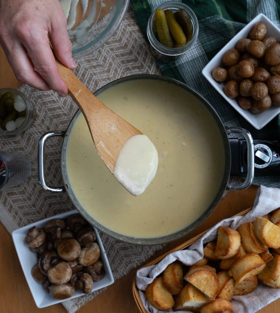 wooden spoon with cheese fondue on it over the melted pot of cheese