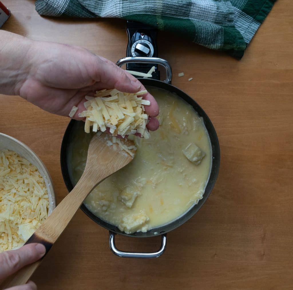 adding cheese to the fondue pot while it melts stirring it with a wooden spoon