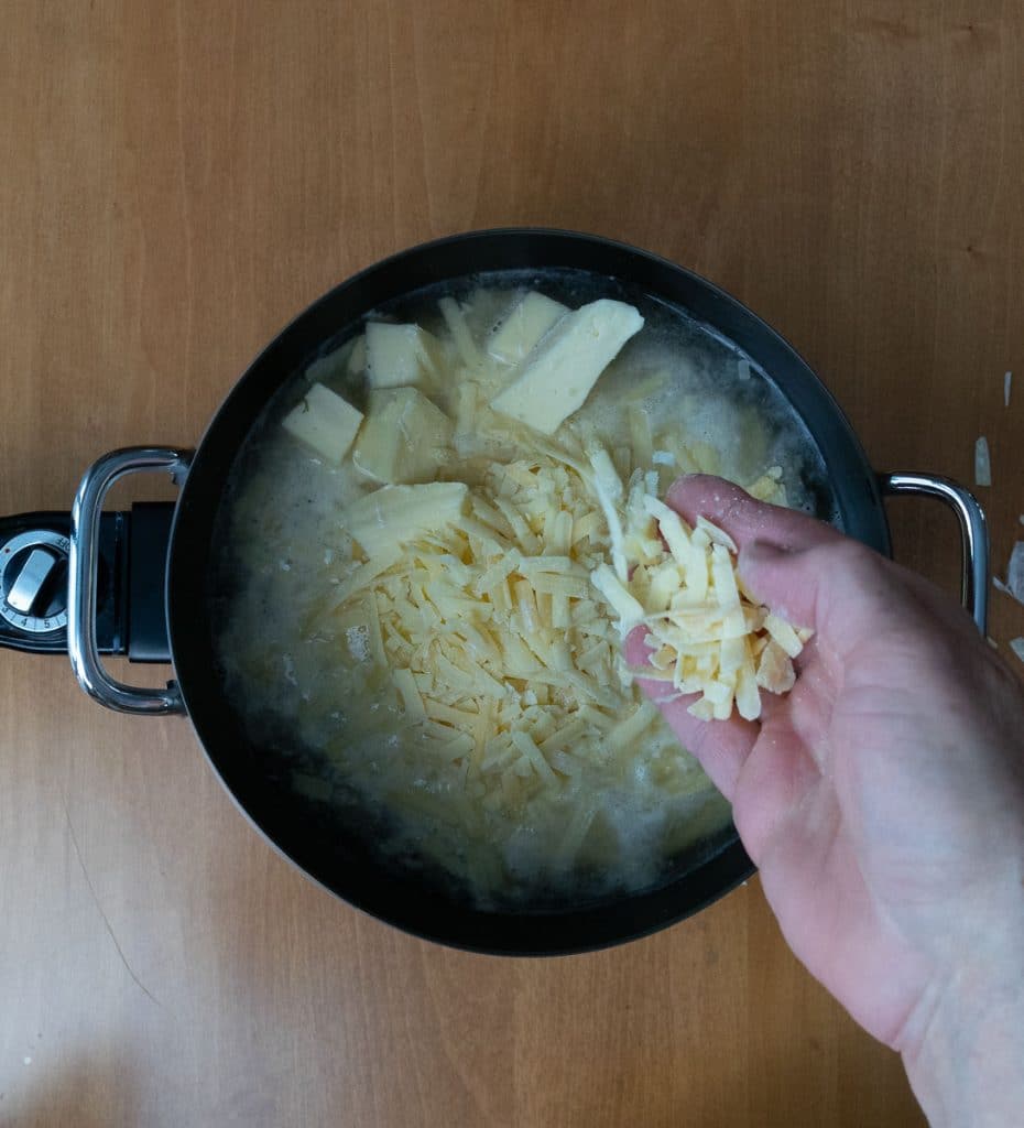 hand adding cheese to the wine and lemon juice in the fondue pot