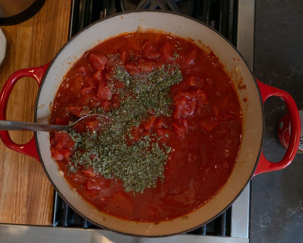 adding herbs to the spaghetti sauce there is spoon in the pan on the stovetop