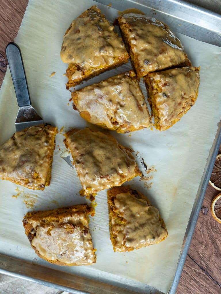 pumpkin loaded scones on a parchment lined baking sheet. the top four scones form a circle the bottom four scones are scattered on the baking sheet one of the scones has a spatula underneath it