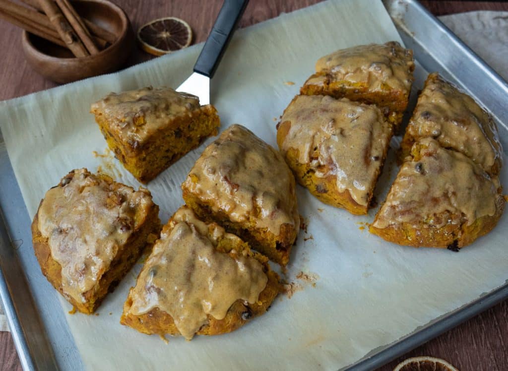 loaded pumpkin scones on a parchment lined baking sheet with a spatula under one of the scones