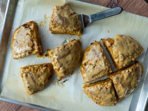loaded pumpkin scones on a parchment lined baking sheet with a spatula under one of the scones