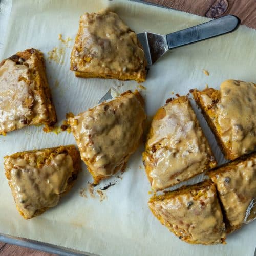 loaded pumpkin scones on a parchment lined baking sheet with a spatula under one of the scones