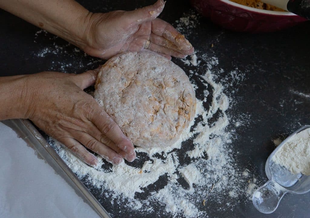 a round shaped scone on a floured counter with two hands shaping it into a round