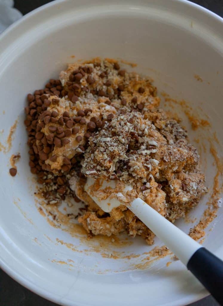 scone dough in white bowl, with a spatula in the bowl with the mix ins or cinnamon chips, candied ginger, and toasted pecans on top of the scone dough